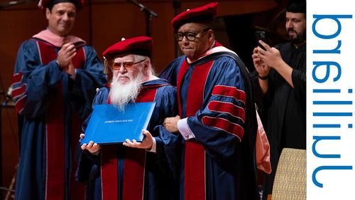 A man with a long beard receiving an honorary degree on a stage